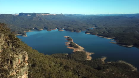 Antena:-Drone-Volando-Junto-A-Una-Cadena-Montañosa-Hacia-Un-Hermoso-Lago-Azul-En-Nueva-Gales-Del-Sur,-Australia