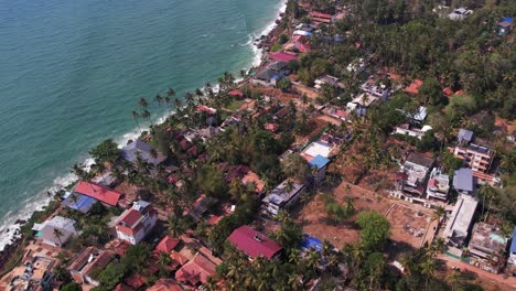 Aerial-drone-shot-of-varkala-beach-filled-with-shops,-buildings-and-trees
