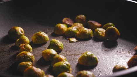 A-close-up-shot-of-marinated-brussels-sprouts-roasting-in-a-hot-frying-pan,-a-chef-holding-a-spatula-carefully-turns-the-sprouts-with-a-wooden-spatula-to-ensure-an-even-cook