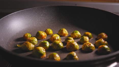 A-close-up-shot-of-a-hand-spaciously-placing-seasoned-and-sliced-brussels-sprouts-onto-a-hot-surface-of-a-ceramic-frying-pan,-the-chef-roasting-the-fresh-vegetables-as-a-healthy-yet-tasty-side-dish