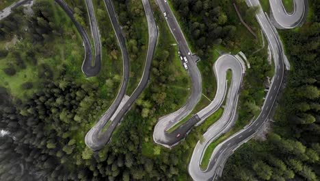 Aerial-flyover-with-birdseye-view-of-the-turns-of-Maloja-Pass-in-Engadin,-Switzerland-with-cars-driving-up-and-down-on-the-road-surrounded-by-trees
