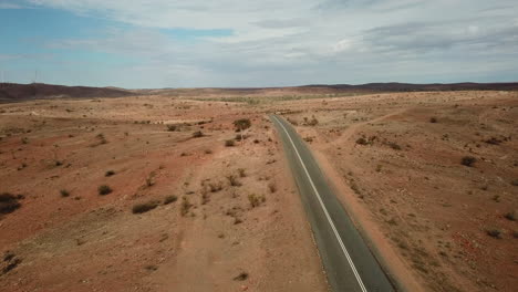 Aerial:-Drone-shot-flying-over-a-solo-highway-in-a-rugged,-empty,-desert-environment-near-Broken-Hill-Australia