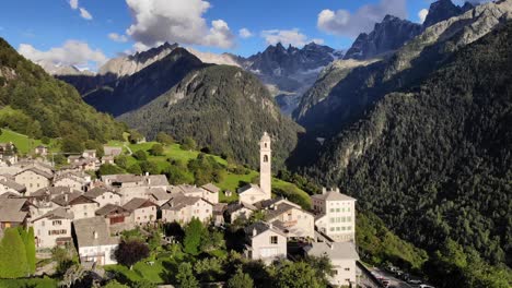 Aerial-flyover-in-the-afternoon-sunshine-over-the-historical-village-of-Soglio-in-the-Bregaglia-region-of-Grissons,-Switzerland-with-a-view-of-the-old-church-and-mountain-peaks-of-Engadin