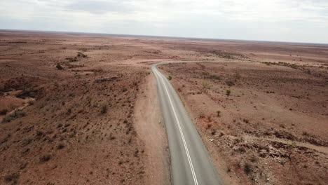 Aerial:-Drone-shot-following-a-deserted-highway-winding-through-a-post-apocalyptic-looking-environment,-near-Broken-Hill-Australia