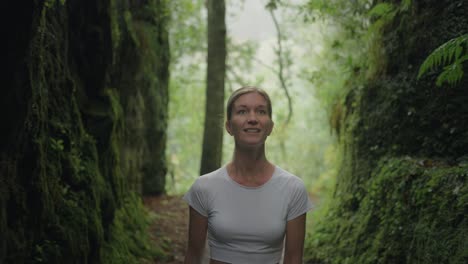 Young-woman-in-white-shirt-walks-through-moss-covered-canyon-mountain-pass,-smiling-and-looking