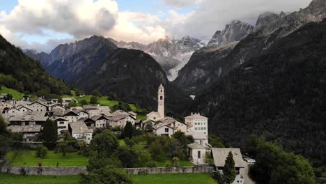 Aerial-flyover-over-the-historical-village-of-Soglio-in-the-Bregaglia-region-of-Grissons,-Switzerland-with-a-view-of-the-old-church-and-mountain-peaks-of-Engadin