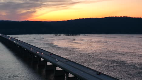 Car-traffic-on-bridge-across-river-during-colorful-orange-sunset