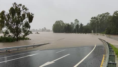 Queensland,-NSW,-Australia,-February-floods---a-deserted-suburban-Brisbane-road-curves-down-and-disappears-into-flood-waters,-as-heavy-rain-continues-to-fall