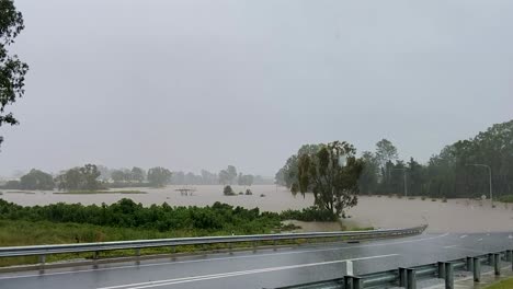Queensland,-NSW,-Australia,-February-floods---a-deserted-suburban-Brisbane-road-curves-down-and-disappears-into-flood-waters-with-torrential-rain-falling-from-grey-skies