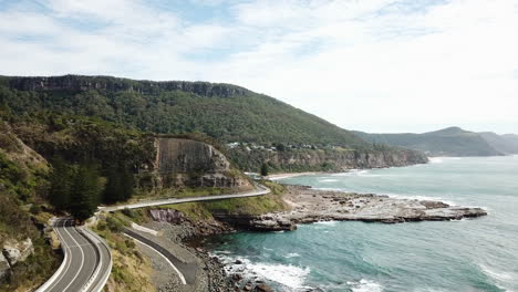 Aerial:-Drone-flying-next-to-a-curvy-highway-between-ocean-and-cliffs,-in-New-South-Wales-Australia
