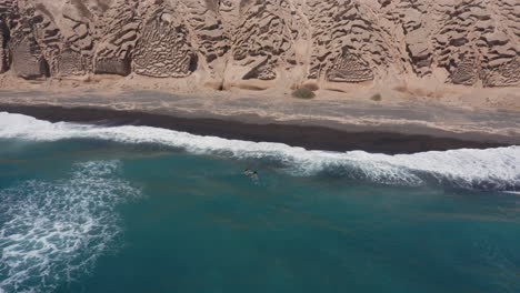 Aerial:-Two-children-swim-in-shallow-water-with-big-waves-in-Vlychada-beach-of-Santorini,-4K-prores
