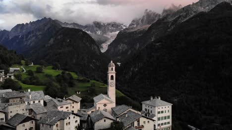Aerial-flyover-over-the-rooftops-of-the-historical-village-of-Soglio-in-the-Bregaglia-region-of-Grissons,-Switzerland-with-a-view-of-the-old-church-and-mountain-peaks-of-Engadin