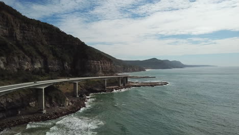 Aerial:-Drone-following-vehicles-driving-across-a-large-bridge-along-a-beautiful-coastline,-in-New-South-Wales-Australia