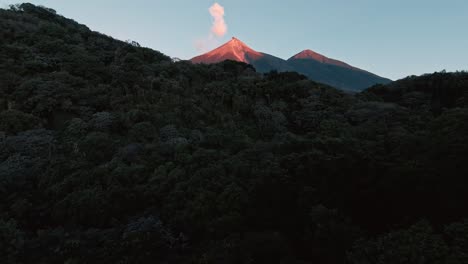 FPV-fly-through-dense-tropical-jungle-revealing-lit-volcano-peak,-aerial-FPV-view