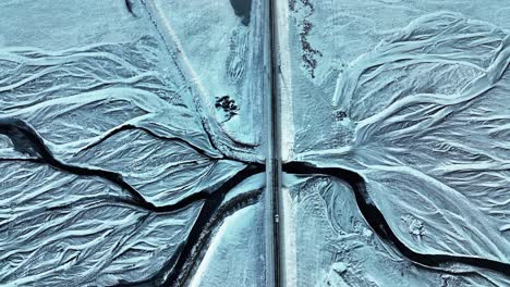 Overhead-aerial-drone-shot-of-a-lone-car-crossing-bridge-over-a-frozen-glacial-river-during-winter-in-South-Iceland