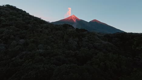 Passing-close-to-tree-tops-towards-sunlit-peak-of-smoking-volcano,-aerial-fpv-view