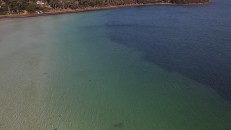 Drone-aerial-pan-up-over-tropical-blue-water-to-show-houses-on-sandy-beach-front