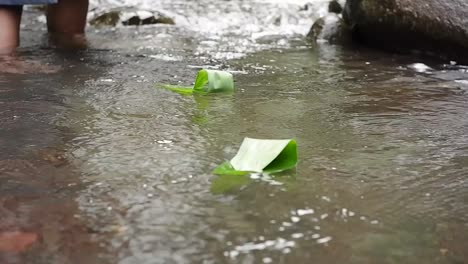 a-man-is-playing-a-boat-made-of-bamboo-leaves-in-a-clear-river