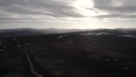 Cinematic-aerial-drone-footage-twisitng-and-rising-above-a-mountain-landscape-and-heather-moorland-with-patches-of-snow-as-the-sun-begins-to-set-behind-the-clouds