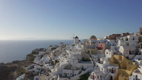 Aerial:-Drone-flies-at-low-altitude-in-Oia-of-Santorini,-Greece-next-to-the-windmills