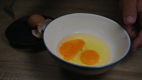Hand-breaking-an-egg-and-then-beats-it-with-another-already-in-the-bowl,-Scrambling-eggs-in-a-bowl