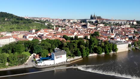 Aerial-flyover-alongside-Vltava-river-in-Praha,-Czech-Republic-with-a-view-of-the-Prague-Castle,-red-roofs-of-Mala-Strana-and-Charles-Bridge-on-a-sunny-morning