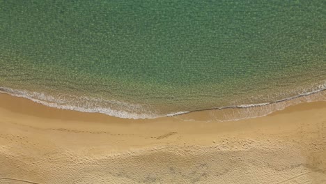 Top-down-view-of-a-clear-water-beach-in-Spain-with-calm-weaves-rolling-into-coastline