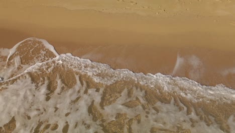 Ocean-waves-white-sea-foam-rolling-into-a-golden-sand-empty-beach-in-Costa-Brava,-Spain