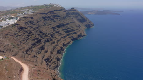 Slow-revealing-aerial-shot-of-Skaros-rock-in-Santorini,-Greece-during-a-sunny-day