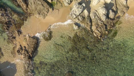 Aerial-top-down-sea-clear-water-waves-break-on-rolling-into-rock-and-sand-beach