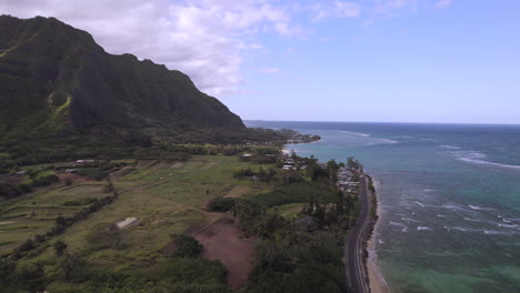Aerial-over-shoreline-in-Oahu,-Hawaii-pushing-down-towards-the-ocean-and-road-winding-along-the-beach