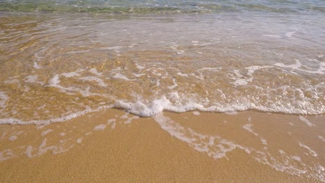 Slow-motion-view-of-gently-clear-water-waves-and-sea-foam-rolling-into-a-beach-sand