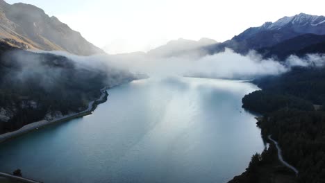 Ein-Sonnenaufgang-überflug-Durch-Die-Wolken-Oben-über-Dem-Silsersee-In-Maloja,-Schweiz-Mit-Blick-Auf-Die-Engadiner-Gipfel-Und-Wolken,-Die-Sich-über-Das-Wasser-Bewegen