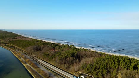 Descending-aerial-shot-of-magnificent-Baltic-Sea-and-driving-cars-on-narrow-road-of-Hel-in-Poland