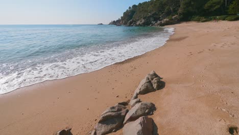 Turquoise-water-waves-rolling-into-a-pink-sand-beach-in-Lloret-de-Mar,-Spain