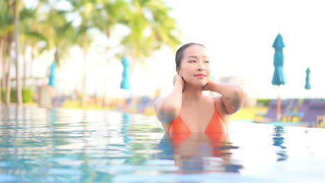 Sexy-asian-woman-in-bikini-in-swimming-pool-caresses-her-wet-hair,-slow-motion