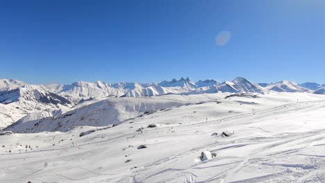 Aerial-shot-of-a-wintersport-area-with-off-piste-skiers'-tracks-in-the-foreground-and-skiers-on-a-prepared-slope-in-the-background