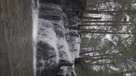 Vertikale-Aufnahme-Eines-Atemberaubenden-Wasserfalls,-Der-In-Zeitlupe-Auf-Felsen-Im-Wald-Kaskadiert