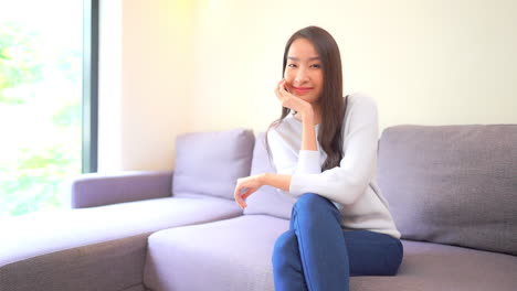 A-young-woman-sitting-on-a-couch-places-her-chin-in-her-hand-and-smiles