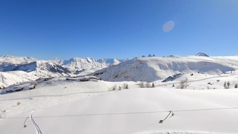 Droneshot-Sobre-Un-Telesilla-Con-Esquiadores-Y-Snowboarders-En-Un-Paisaje-Nevado-De-Montaña-Invernal,-En-La-Estación-De-Esquí-Les-Sybelles-En-Los-Alpes-Franceses