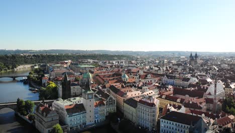 Aerial-pan-around-the-city-of-Praha,-Czech-Republic-from-up-above-the-Vltava-river-with-a-view-of-the-rooftops-of-Old-Town,-various-towers-and-spires,-Charles-Bridge-and-the-Prague-Castle