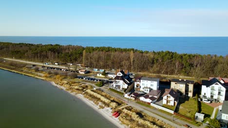 Aerial-drone-shot-of-beautiful-narrow-island-of-Hel-with-road,houses-and-forest-trees-during-sunny-day---Blue-Baltic-Sea-in-background
