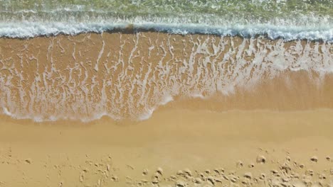 Waves-rolling-into-a-golden-sand-beach,-aerial-top-down-view