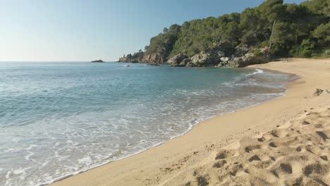 Clear-water-waves-rolling-into-a-sandy-exotic-beach-in-Lloret-de-mar,-Spain