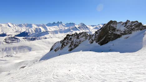Toma-Aérea-Del-Paisaje-Montañoso-Cubierto-De-Nieve-Con-Formaciones-Rocosas-Y-Pistas-De-Esquiadores-En-Primer-Plano