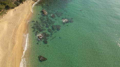 Aerial-view-sunny-over-calm-beach-in-Costa-Brava,-Spain,-very-clear-water