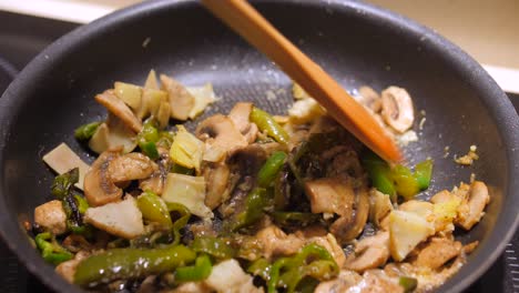 Close-up-view-of-stir-fry-vegetables-with-wooden-tea-spoon-consisting-of-pepper,-mushroom,-garlic-and-rosemary-in-the-kitchen