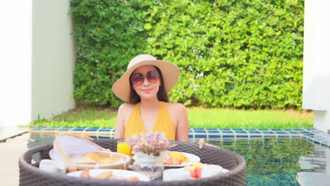 Smiling-Exotic-Woman-With-Breakfast-on-Floating-Plate-in-Swimming-Pool-of-Luxury-Private-Villa-in-Tropical-Destination,-Slow-Motion