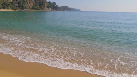 Klare-Wasserwellen-Und-Meeresschaum-Rollen-In-Den-Strand-Von-Santa-Cristina,-Spanien,-Zeitlupe