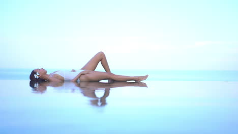Exotic-Woman-in-Tropical-Paradise,-Lying-on-Infinity-Pool-Border-Colliding-With-Sea-Horizon-and-Sky
